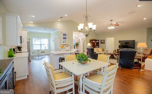 dining room with ceiling fan with notable chandelier, dark hardwood / wood-style floors, and vaulted ceiling