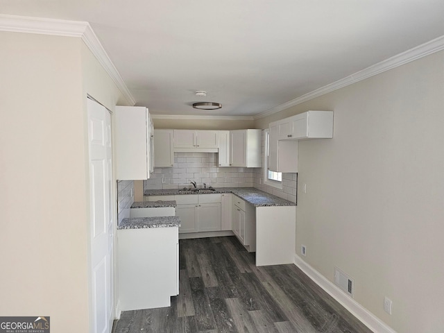 kitchen with dark hardwood / wood-style flooring, backsplash, dark stone counters, ornamental molding, and white cabinets