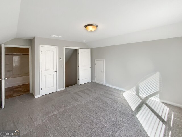 unfurnished bedroom featuring carpet flooring, ensuite bath, and lofted ceiling