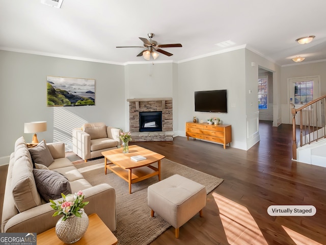 living room with dark hardwood / wood-style floors, ceiling fan, a stone fireplace, and crown molding