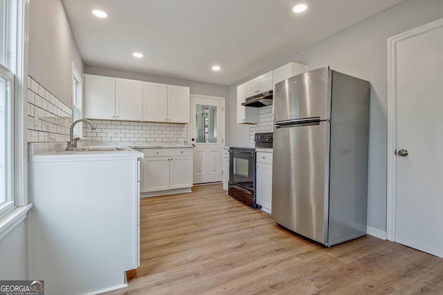 kitchen featuring white cabinets, sink, stainless steel fridge, light wood-type flooring, and black range with electric cooktop