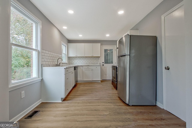 kitchen featuring plenty of natural light, white cabinetry, stainless steel appliances, and light hardwood / wood-style flooring