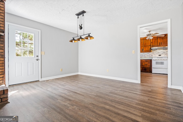 unfurnished dining area featuring ceiling fan, baseboards, dark wood-style flooring, and a textured ceiling