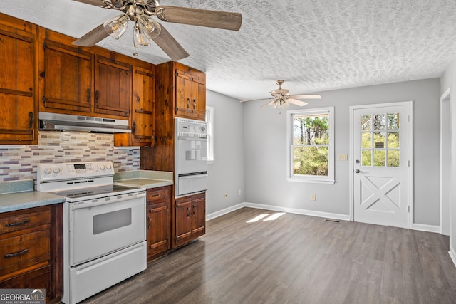 kitchen with dark wood-type flooring, under cabinet range hood, light countertops, decorative backsplash, and white appliances