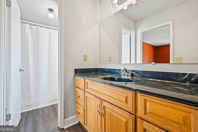 full bath featuring a textured ceiling, wood finished floors, a shower with shower curtain, baseboards, and vanity