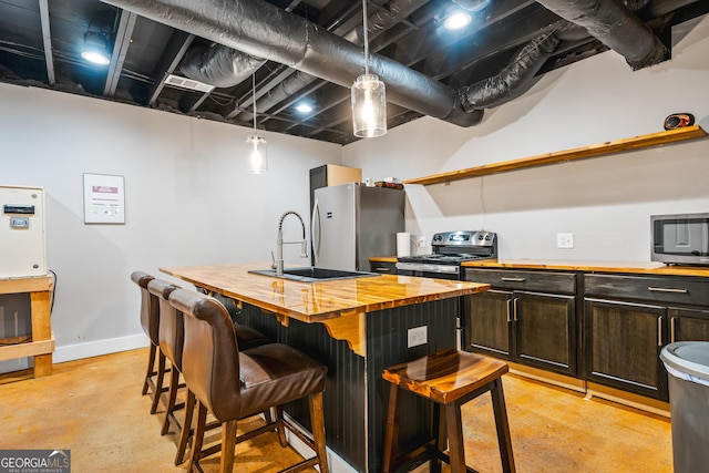 kitchen featuring a kitchen bar, a center island with sink, finished concrete floors, stainless steel appliances, and wooden counters