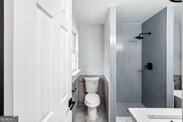 bathroom with a tile shower, vanity, toilet, and tile walls