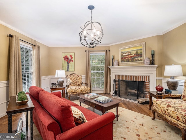 living area with a notable chandelier, ornamental molding, a brick fireplace, wainscoting, and wood finished floors