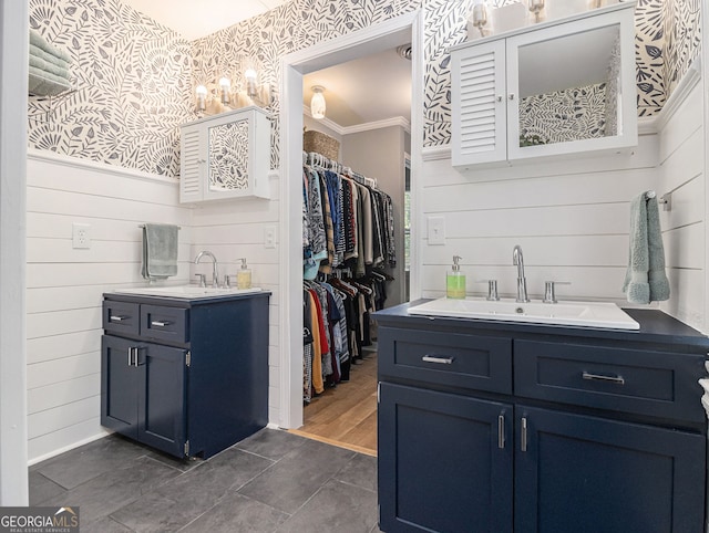 full bathroom featuring a walk in closet, two vanities, ornamental molding, a sink, and wallpapered walls