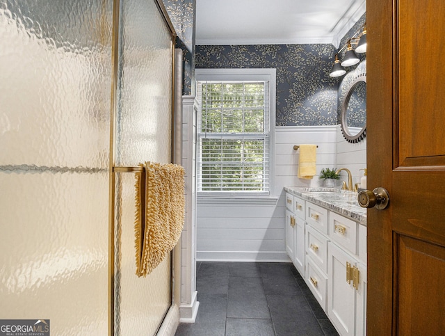 bathroom featuring tile patterned flooring, a shower with shower door, a wainscoted wall, vanity, and wallpapered walls