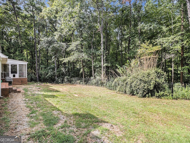 view of yard featuring a forest view, a sunroom, and fence