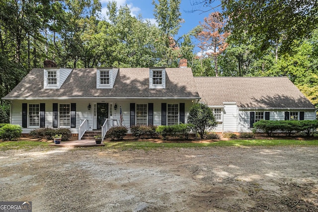 cape cod-style house with a shingled roof, covered porch, and a chimney