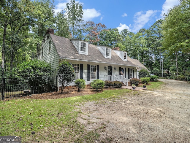 new england style home with a shingled roof, a chimney, a front yard, and fence