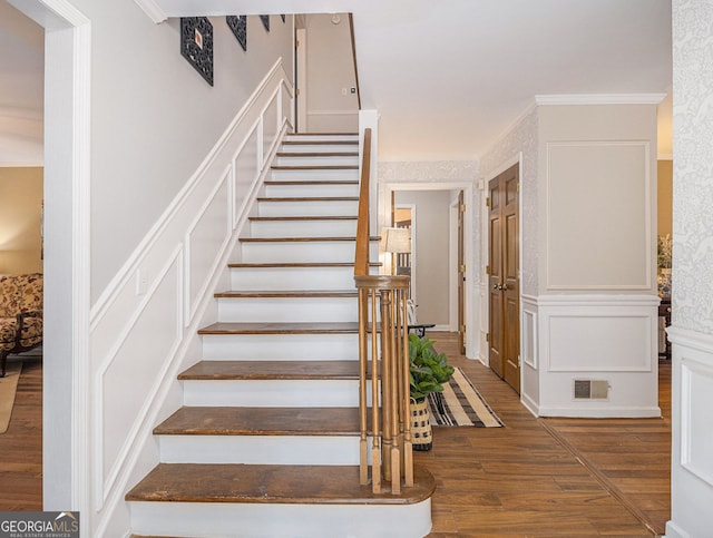 stairs featuring ornamental molding, wood finished floors, visible vents, and a decorative wall