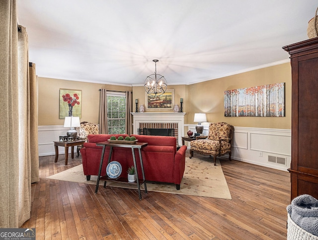 living room featuring visible vents, dark wood-type flooring, crown molding, a brick fireplace, and a chandelier