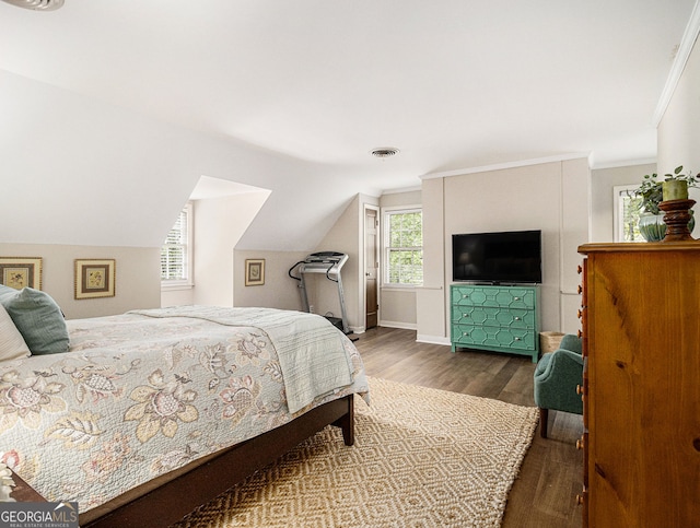 bedroom featuring wood finished floors, visible vents, baseboards, vaulted ceiling, and crown molding