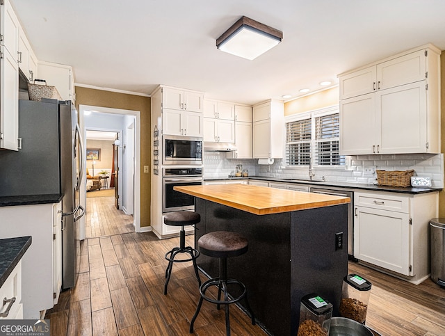 kitchen featuring dark wood-style floors, a breakfast bar, stainless steel appliances, butcher block countertops, and under cabinet range hood