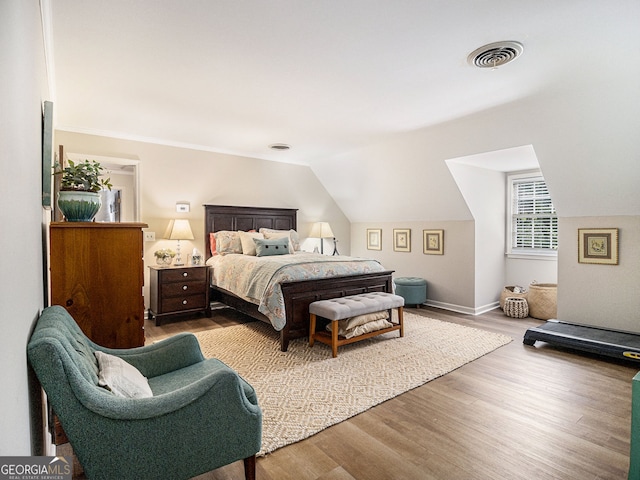 bedroom with vaulted ceiling, wood finished floors, visible vents, and baseboards