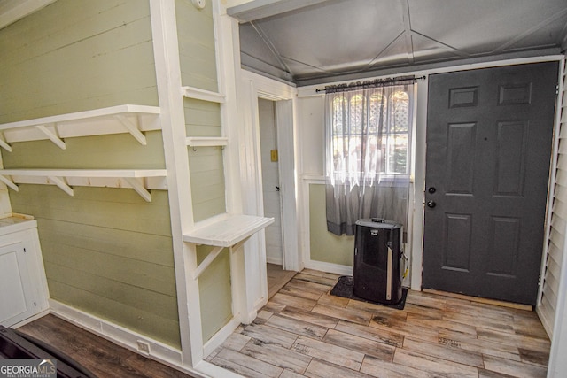 entrance foyer featuring light wood-type flooring, vaulted ceiling, and wooden walls