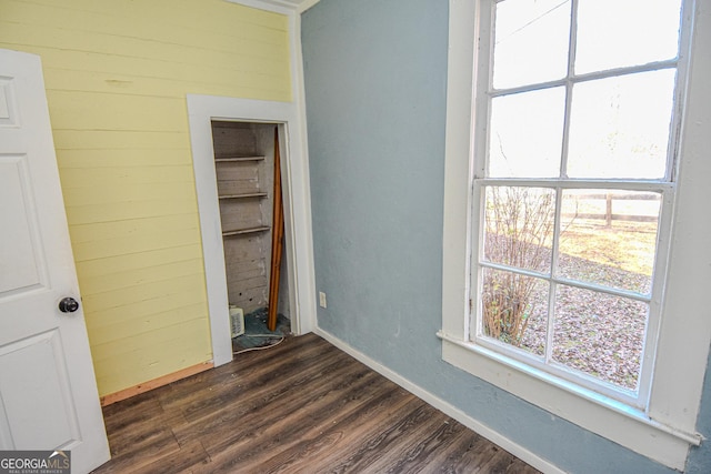 unfurnished bedroom with wooden walls, a closet, and dark wood-type flooring