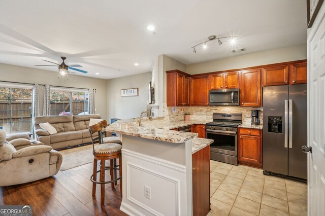 kitchen with light stone counters, decorative backsplash, appliances with stainless steel finishes, a peninsula, and a kitchen bar