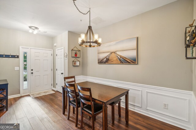 dining area with dark wood-style flooring, a wainscoted wall, and an inviting chandelier