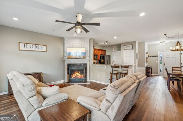 living area with baseboards, dark wood finished floors, a high end fireplace, ceiling fan with notable chandelier, and recessed lighting