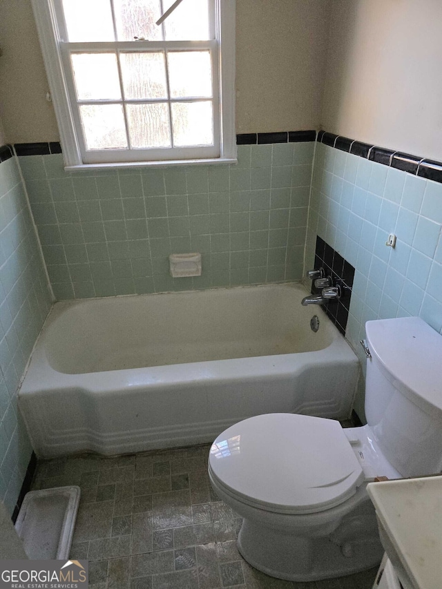 bathroom featuring a bathing tub, vanity, tile walls, and toilet