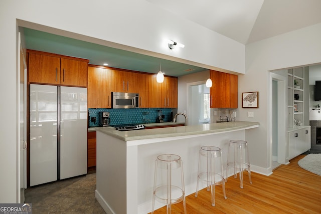 kitchen featuring hanging light fixtures, stainless steel appliances, a kitchen breakfast bar, kitchen peninsula, and hardwood / wood-style floors