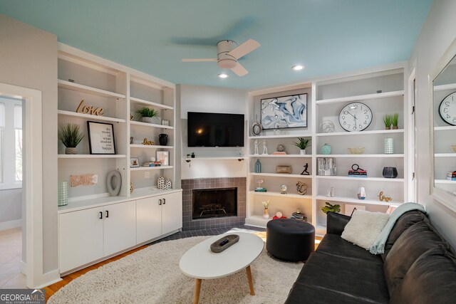 living room with ceiling fan, built in shelves, a tile fireplace, and light hardwood / wood-style flooring