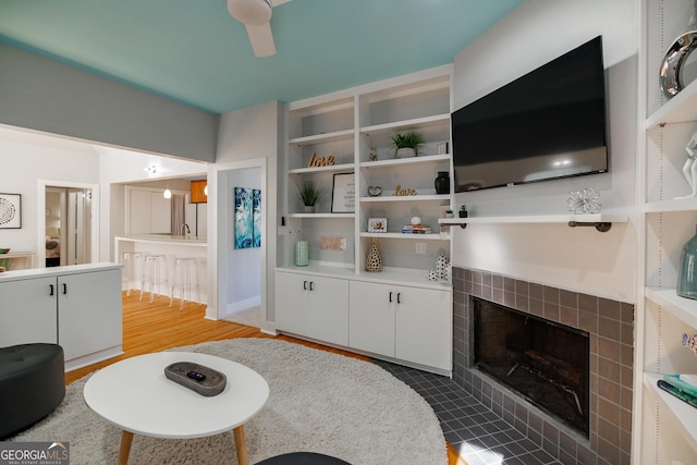 living room featuring a tiled fireplace, ceiling fan, hardwood / wood-style floors, and built in features