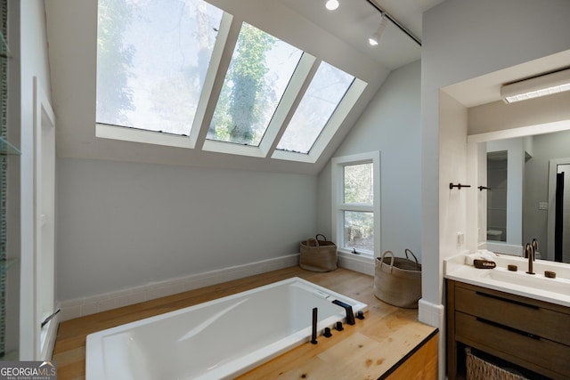 bathroom featuring rail lighting, a bathtub, vanity, lofted ceiling with skylight, and wood-type flooring