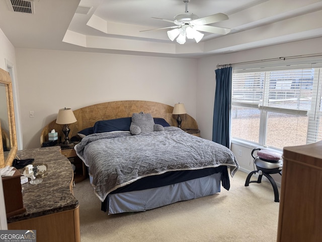 carpeted bedroom with ceiling fan and a raised ceiling