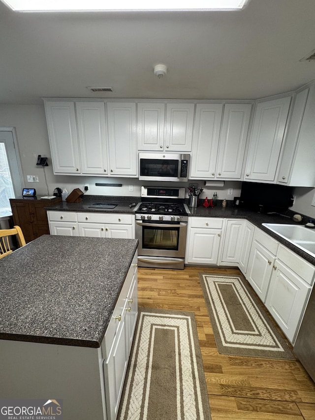 kitchen featuring sink, a kitchen island, light hardwood / wood-style floors, white cabinetry, and stainless steel appliances