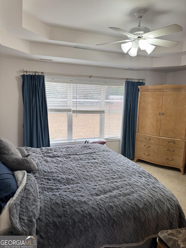 carpeted bedroom featuring a tray ceiling and ceiling fan