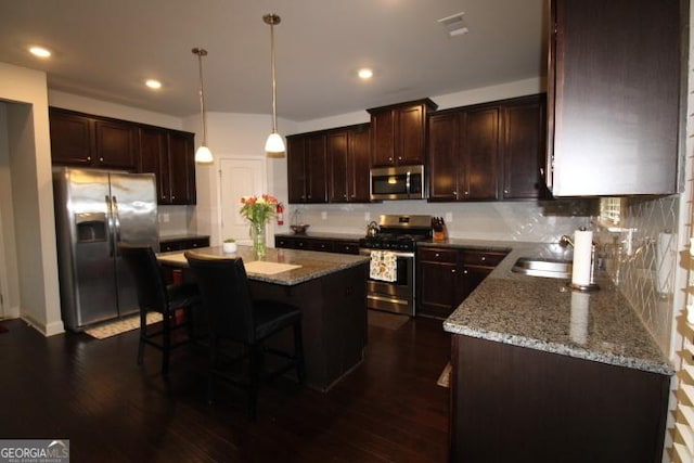 kitchen featuring dark hardwood / wood-style flooring, stainless steel appliances, a kitchen island, and hanging light fixtures