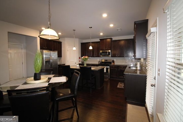 kitchen with backsplash, stainless steel appliances, decorative light fixtures, dark hardwood / wood-style floors, and a kitchen island