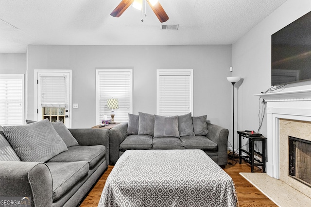 living room featuring a high end fireplace, a textured ceiling, ceiling fan, a healthy amount of sunlight, and hardwood / wood-style flooring