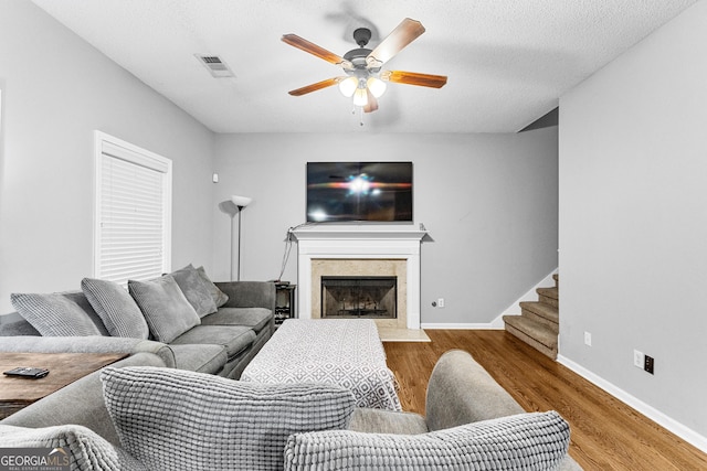 living room with ceiling fan, a fireplace, wood-type flooring, and a textured ceiling