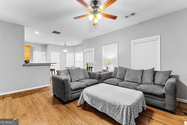 living room featuring ceiling fan, light wood-type flooring, and a textured ceiling