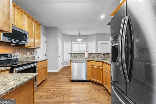 kitchen with backsplash, light stone countertops, appliances with stainless steel finishes, decorative light fixtures, and light hardwood / wood-style floors