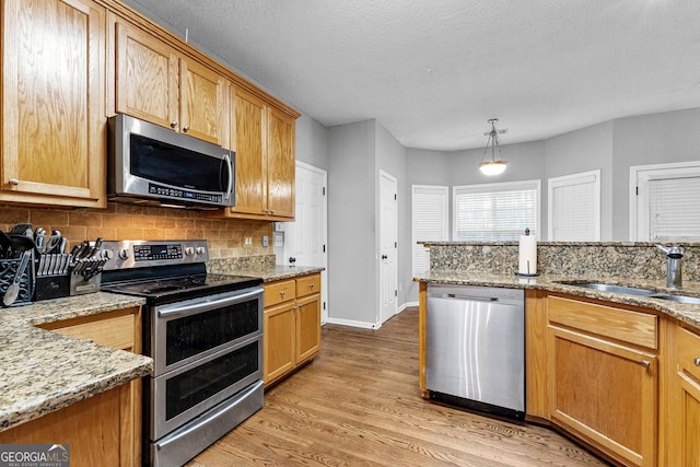 kitchen with appliances with stainless steel finishes, light stone counters, sink, pendant lighting, and light hardwood / wood-style floors