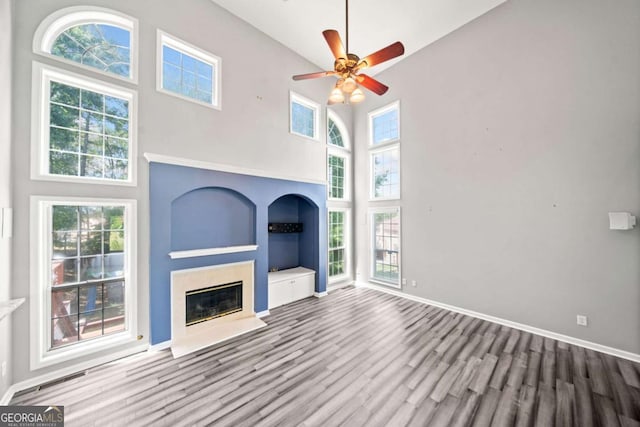 unfurnished living room with hardwood / wood-style floors, a towering ceiling, and ceiling fan