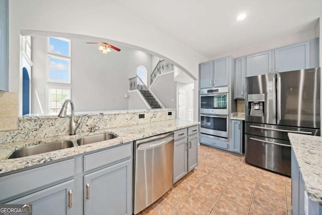 kitchen with appliances with stainless steel finishes, light stone counters, ceiling fan, and sink