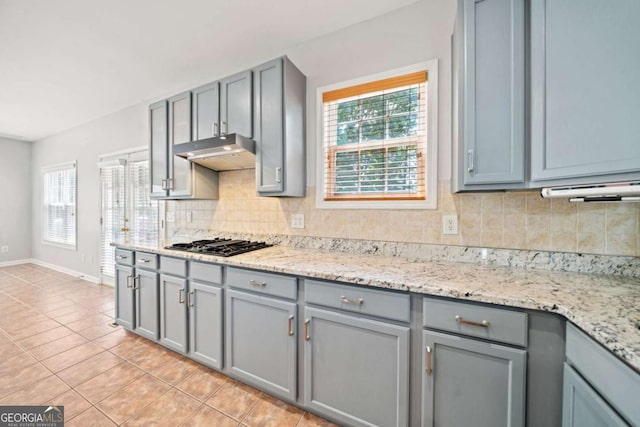 kitchen featuring stainless steel gas stovetop, decorative backsplash, gray cabinets, and light stone countertops