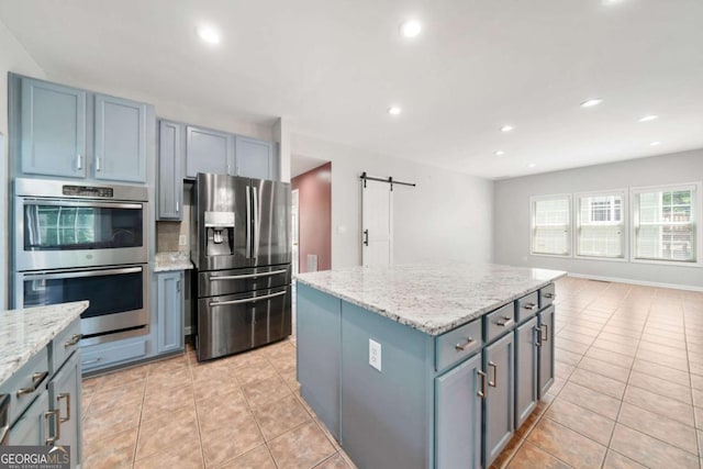 kitchen featuring stainless steel appliances, a kitchen island, a barn door, light stone counters, and light tile patterned flooring