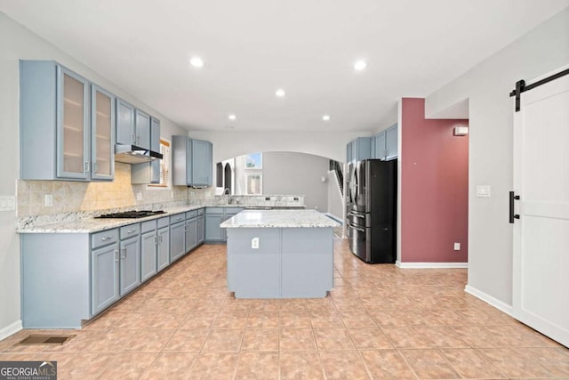 kitchen with a center island, a barn door, light stone countertops, and appliances with stainless steel finishes