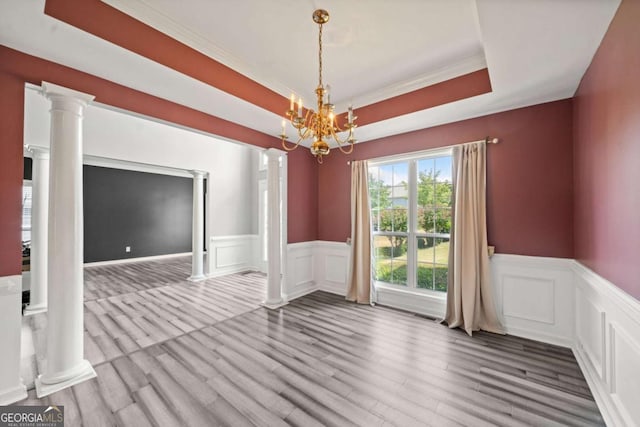 empty room featuring ornate columns, a raised ceiling, a chandelier, hardwood / wood-style flooring, and ornamental molding