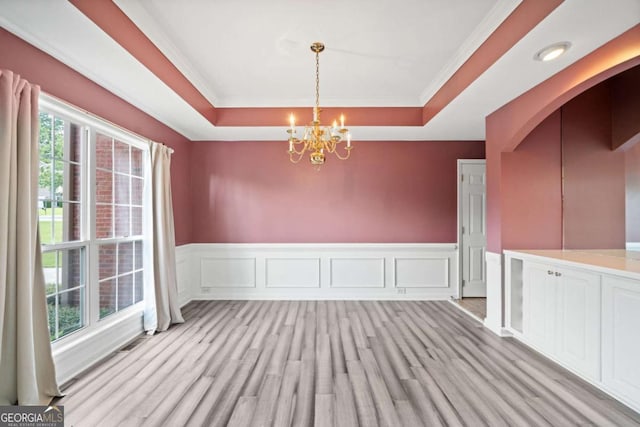 unfurnished dining area with an inviting chandelier, light hardwood / wood-style flooring, a raised ceiling, and crown molding