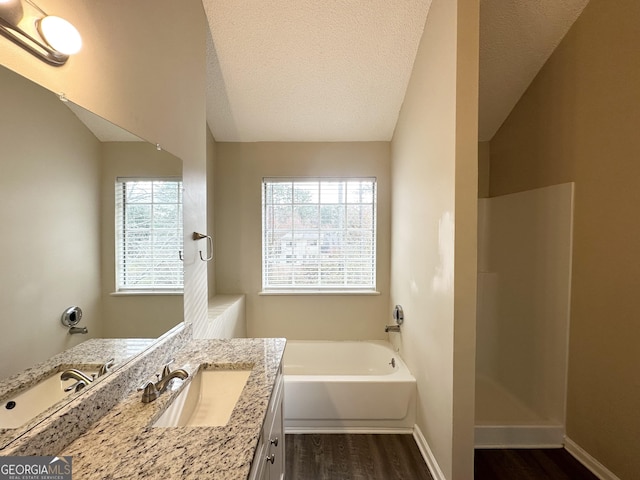 bathroom with a bathing tub, lofted ceiling, wood-type flooring, and a textured ceiling